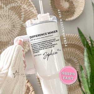 May include: A white stainless steel tumbler with a handle, a clear lid, and a straw. The tumbler features black printed text that defines the term DIFFERENCE MAKER, followed by the name Sophia in a script font and two small heart icons.