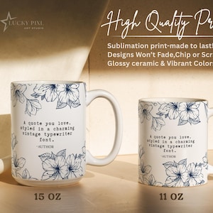 May include: Two white ceramic mugs, one 15 oz and one 11 oz, featuring a dark blue floral pattern and the text: A quote you love, styled in a charming vintage typewriter font. -AUTHOR. The mugs have a glossy finish and a handle on the right side.