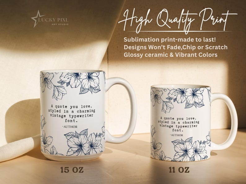 May include: Two white ceramic mugs, one 15 oz and one 11 oz, featuring a dark blue floral pattern and the text: A quote you love, styled in a charming vintage typewriter font. -AUTHOR. The mugs have a glossy finish and a handle on the right side.