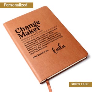 May include: A tan leather-textured notebook featuring the black printed text Change Maker [cheynj mey-ker] noun, a definition of the term, the phrase Also known as:, and the name Laila in a cursive script font on the front cover.
