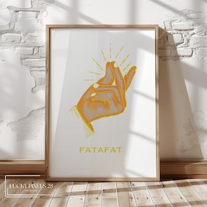 Pode incluir: Impressão artística emoldurada com um gesto de mão laranja e cinza com linhas radiantes. A palavra "FATAFAT" está impressa em amarelo abaixo. A obra de arte está em um fundo branco, em uma moldura de madeira.