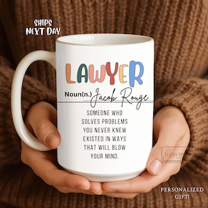 May include: White ceramic mug with the word "LAWYER" in colorful letters. The mug includes the name "Jacob Rouge" and a definition of a lawyer. The mug is held by a person.