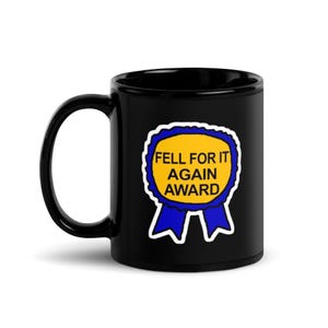 Peut inclure: Mug à café noir avec un graphique "Fell For It Again Award" bleu et jaune. Le prix a la forme d'un ruban avec le texte en gras. La tasse a une poignée incurvée.