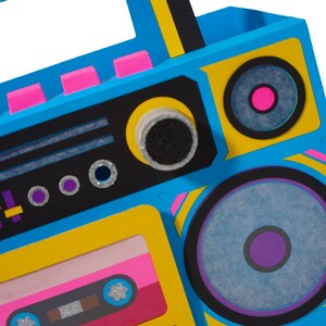 May include: A colorful, retro-style boombox with a vibrant design. The boombox features a blue body with yellow and black accents, pink details, and a cassette tape. The speakers have purple and pink centers.