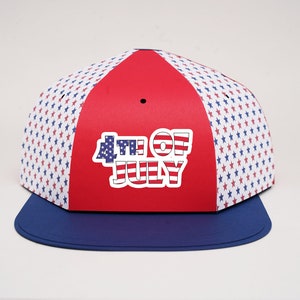 Puede incluir: Gorra de béisbol roja, blanca y azul con el texto "4th of July". La gorra presenta un panel central rojo y un panel blanco con estrellas azules y rojas. La visera es de color azul liso.