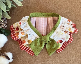 Pode incluir: Uma coleira decorativa para animais de estimação com laço e acabamento de bolinhas verdes. A coleira tem acabamento em renda branca e tecido estampado com folhas de outono e detalhes em vermelho. O interior é listrado.