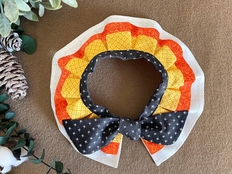 May include: A black and white bow tie with a yellow and orange patterned collar. The collar has a ruffled edge.