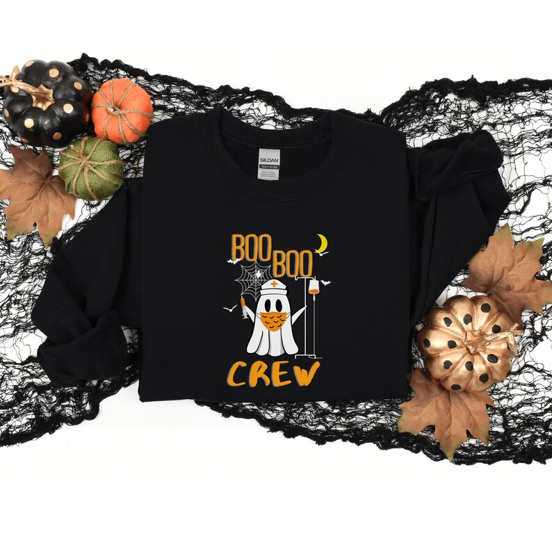 May include: Black sweatshirt with a white ghost wearing a face mask and a nurse's hat. The ghost is holding a syringe and an IV bag. The text "BOO BOO CREW" is printed in orange on the sweatshirt.