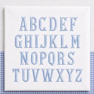 Könnte beinhalten: Ein quadratisches weißes Stoffpaneel mit dem vollständigen Alphabet, das mit hellblauem Garn gestickt ist. Die Buchstaben sind in vier Reihen angeordnet und zeigen Großbuchstaben von A bis Z in einer klassischen Serifenschrift mit Stickerei.
