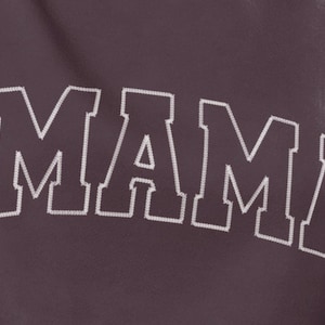 Puede incluir: Una sudadera morada con la palabra "MAMA" bordada en blanco en la parte delantera.