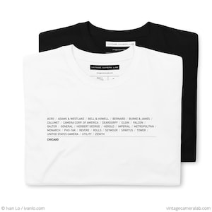 Könnte beinhalten: Zwei T-Shirts, eines weiß und eines schwarz, mit einer Liste von Vintage-Kameramarken, die auf der Vorderseite aufgedruckt sind. Der Text lautet: "ACRO/ADAMS & WESTLAKE/BELL & HOWELL/BERNARD/BURKE & JAMES/CALUMET/CAMERA CORP. OF AMERICA/DEARDORFF/ELGIN/FALCON/GALTER/GENERAL/HERBERT GEORGE/HEROLD/IMPERIAL/METROPOLITAN/MONARCH/PHO-TAK/REVERE/ROLLS/SEYMOUR/SPARTUS/TOWER/UNITED STATES CAMERA/UTILITY/ZENITH CHICAGO"