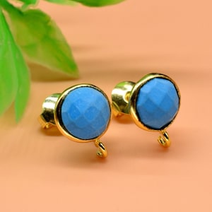 May include: A pair of gold stud earrings with light blue faceted gemstone accents. The earrings have a small loop on the bottom.