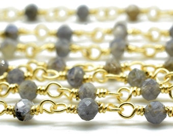 May include: Close-up of several strands of gold-colored chain necklaces. Each chain features small, faceted gray beads interspersed along the length. The chains are arranged parallel to each other, creating a layered effect against a white background. Jewelry.