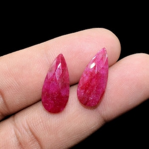 Puede incluir: Dos piedras preciosas rojas en forma de lágrima con un corte facetado. Las piedras preciosas se sostienen en una mano.