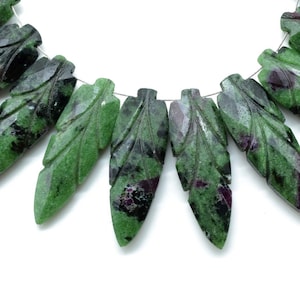 May include: A strand of green and pink gemstone beads carved into leaf shapes. The beads are strung on a silver wire.