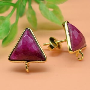 以下が含まれることがあります： ピンクの宝石のアクセントが付いた、ゴールドの三角形のイヤリングのペア。イヤリングはポストバックと底に小さなループが付いています。