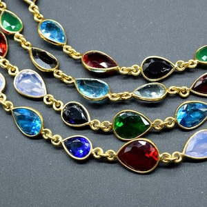 以下が含まれることがあります： 青、緑、赤、黒など、さまざまな色の涙滴型の宝石がついた、マルチストランドネックレス。ネックレスは金色の金属製です。