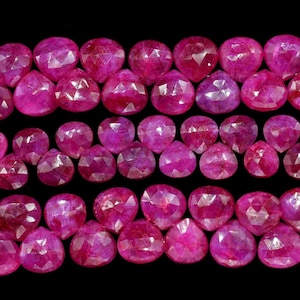 Può includere: Una collana di perle di rubino, ogni perla è sfaccettata e ha un colore rosa intenso. Le perle sono disposte in tre file, con la fila superiore leggermente sfalsata rispetto alle due file inferiori.