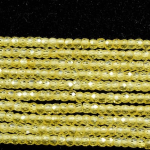 Puede incluir: Una hebra de cuentas de vidrio amarillo facetadas. Las cuentas son pequeñas y redondas, y tienen una superficie brillante y reflectante.