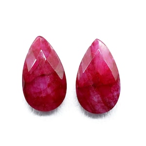 Może przedstawiać: Dwa czerwone koraliki z kamieni szlachetnych w kształcie łzy z fasetowanym wzorem.