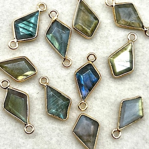 May include: A collection of gemstone pendants with a diamond shape and gold-colored metal trim. The gemstones have a variety of colors, including blue, green, and gray. Each pendant has a small loop at the top for attaching to a chain or other jewelry component.