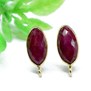 May include: A pair of gold earrings with red gemstone oval-shaped studs.
