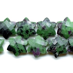 Könnte beinhalten: Eine Strähne aus sternförmigen Edelsteinperlen in Grün, Schwarz und Lila. Die Perlen sind facettiert und haben eine natürliche, raue Textur.