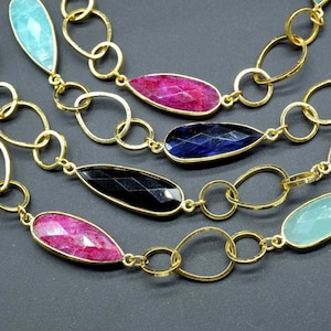 以下が含まれることがあります： 青い、ピンク、緑、黒など、さまざまな色の涙の形をした宝石がついた金のチェーンネックレスです。