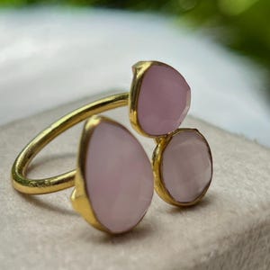 May include: A gold ring with three pink teardrop-shaped stones. The ring is on a white surface.