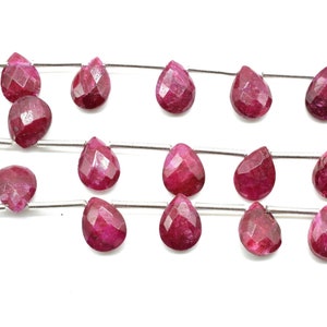 May include: A strand of faceted ruby gemstone beads in a teardrop shape. The beads are strung on a silver wire.