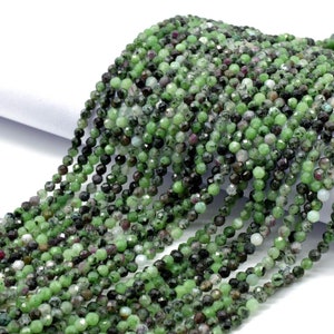May include: A strand of green, faceted gemstone beads. The beads are small and round, and they have a slightly irregular shape. The beads are strung on a clear thread.