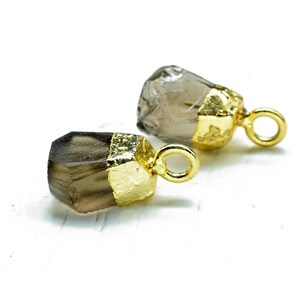 May include: Two smoky quartz crystal pendants with gold-plated caps and jump rings. The crystals are faceted and have a natural, raw look.