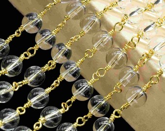 Puede incluir: Una hebra de cuentas de vidrio transparentes enhebradas en una cadena dorada. Las cuentas son redondas y tienen un ligero brillo.