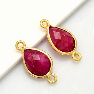 Puede incluir: Dos colgantes de forma de lágrima de color dorado con inserciones de piedras preciosas rojas. Cada colgante tiene dos anillos de salto para sujetar a las joyas.