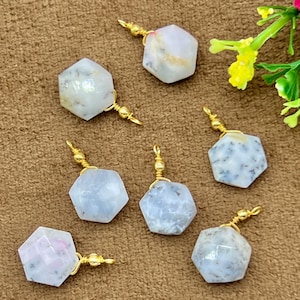 May include: Seven hexagonal gemstone pendants with gold-colored wire detailing. The gemstones are primarily white and gray, with some showing hints of pink and blue. The pendants are arranged on a brown surface.