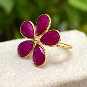 May include: A gold ring with a pink flower design. The flower has five petals and a gold center.