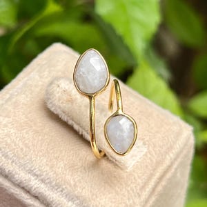 May include: A gold ring with two white moonstone stones. The ring is designed to be worn on the middle finger.