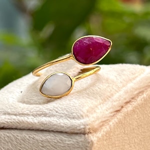 May include: A gold ring with a white and a pink gemstone. The ring is designed to wrap around the finger.