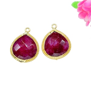 Puede incluir: Dos colgantes de forma de lágrima de color dorado con inserciones de piedras preciosas rojas.