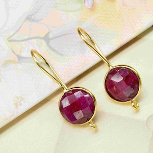 Könnte beinhalten: Ein Paar goldene Ohrringe mit roten Edelstein-Tropfen. Die Ohrringe haben ein schlichtes Design mit einer kleinen Schlaufe oben zum Anbringen an einen Ohrringhaken.