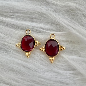 May include: Two gold-toned pendant charms featuring red oval-shaped glass stones. Each charm has a small loop at the top for attaching to a necklace or bracelet.