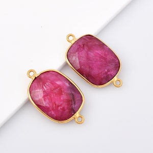 May include: Two gold-toned rectangular gemstone connectors with a pink ruby-like stone in the center. The connectors have two loops on each side for attaching to jewelry.