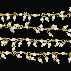 May include: Gold-colored wire strands with white, marble-like beads. The beads are clustered in small groups, creating a delicate, cascading effect. The jewelry component is set against a black background.
