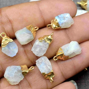 May include: A collection of rainbow moonstone pendants with gold-plated settings. The stones are raw and have a natural, irregular shape. The pendants are perfect for jewelry making or crafting.