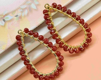 May include: A pair of gold-toned earrings with a teardrop shape. The earrings are made with small, red beads that are strung together in a circular pattern.