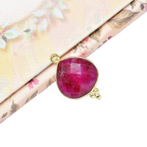 May include: A teardrop-shaped pendant with a deep red gemstone set in gold. The pendant has a small gold bead accent on the side.