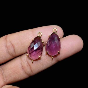 Può includere: Due ciondoli a forma di goccia di ametista con montature dorate. I ciondoli sono sfaccettati e hanno una tonalità viola.
