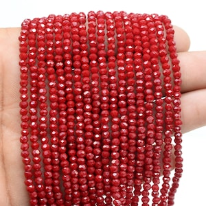 May include: A strand of red faceted glass beads. The beads are small and round, and they are strung on a clear thread.