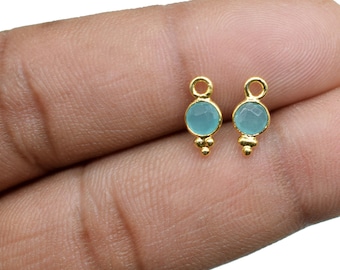 May include: Two gold-toned earring charms with a light blue round gemstone. Each charm has three small gold beads hanging from the bottom.