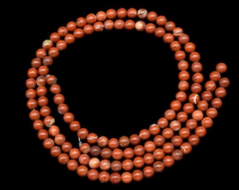 Puede incluir: Cadenas de cuentas de piedra preciosa de jaspe rojo. Las cuentas redondas están pulidas y tienen un color marrón rojizo intenso con algunas variaciones más claras. Están ensartadas para crear un collar o pulsera.